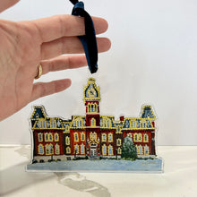 Load image into Gallery viewer, Acrylic ornament of the West Virginia University building, Woodburn Hall  with Christmas lights against a blue background.  Original artwork by artist Emily Kurth.