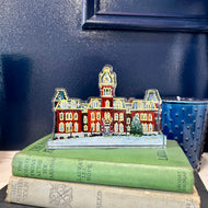 Acrylic cutout of the West Virginia University building, Woodburn Hall with Christmas lights against a blue background.  Original artwork by artist Emily Kurth.