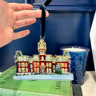 Acrylic ornament of the West Virginia University building, Woodburn Hall with Christmas lights against a blue background.  Original artwork by artist Emily Kurth.