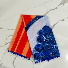 Load image into Gallery viewer, Decorative tea towel with blueberries on light and dark orange striped background design on marled surface.