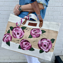 Load image into Gallery viewer, Person holding a tote bag with hand painted pink rose floral design against a white brick wall.