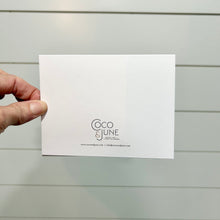 Load image into Gallery viewer, Someone holding a greeting card showing the back with the logo of Coco and June.