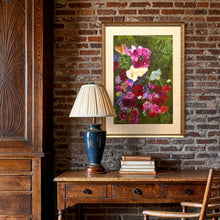 Load image into Gallery viewer, A framed floral painting hangs on a rustic brick wall above a wooden console table with a blue lamp and books. The painting features a dense bouquet of pink, purple, red, yellow, and white flowers with green leaves, set in a gold frame.