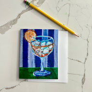 Card with a painting of a cocktail glass with ice and an orange slice,on a blue striped background. Artwork by artist Emily Kurth.