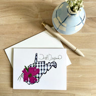 Greeting card with pink rhododendron floral design and navy gingham pattern West Virginia on a wooden surface with a pen and small plant.
