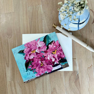 Notecard of pink rhododendrons with a pen and small vase on a wood table